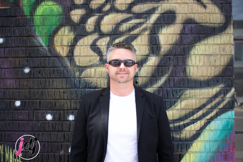 A man in sunglasses standing in front of a wall with graffiti, captured by a Denver DJ at a photo booth rental.