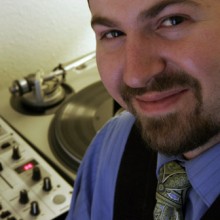 John Murray, a man wearing a tie, is standing in front of a turntable.