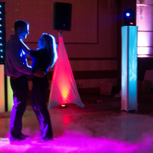 A man and woman dancing in a room with colorful lights at a bat mitzvah.
