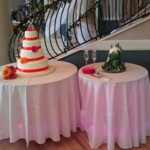 A three tier cake on a table in front of a staircase.