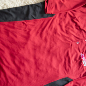 An apparel item, a red and black polo shirt, on a rug.