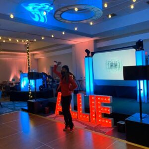 A person standing on a stage with a sign that says "allie'' for bar mitzvah or bat mitzvah pictures.