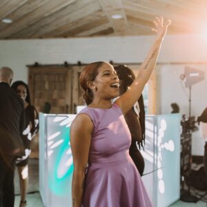 A woman in a purple dress is waving her arms in the air at a wedding reception.
