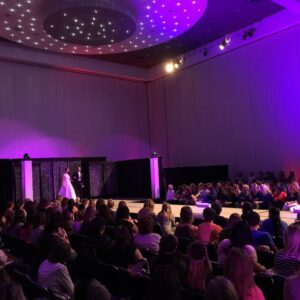 A group of people watching a fashion show on a stage equipped with DJ equipment.