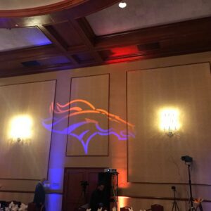 The Denver Broncos logo is projected on the wall using equipment.
