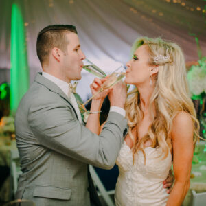 A bride and groom sharing a glass of wine at their wedding reception, with background music provided by a DJ service.