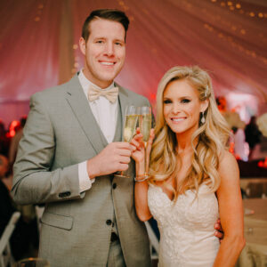 A bride and groom holding champagne glasses in a tent with a photo booth rental.
