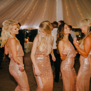 A group of bridesmaids dancing in a tent, enjoying the wedding DJ's music.