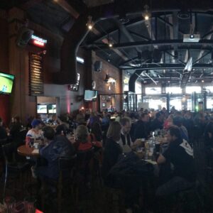A crowd of people participating in live trivia games at tables in a bar.