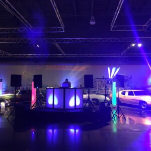 A dance DJ set up in a room with a lot of cars at a school dance.