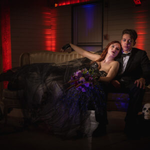 A bride and groom posing on a couch in a dark room with their wedding DJ.