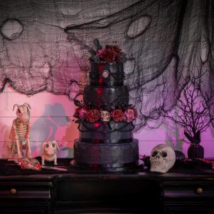 A black cake on a table with skeletons on it for a bat mitzvah.