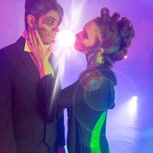 A man and woman in a costume kissing in a dark room, illuminated by the vibrant lights from a Denver DJ service.