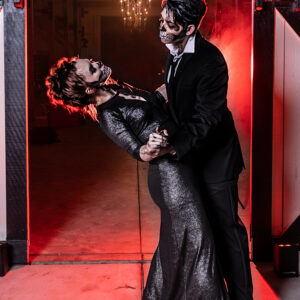 A man and woman in a black dress are dancing in front of a red door at a wedding.