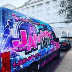 A blue and purple van, offering photo booth rental services, parked in front of a hotel.