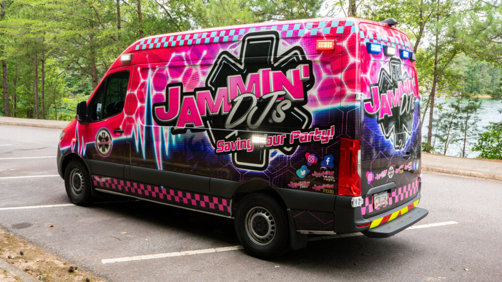 A pink and black van, serving as a photo booth rental, parked in a parking lot.