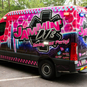A pink and black van, serving as a photo booth rental, parked in a parking lot.