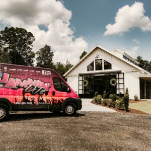 A pink van, offering photo booth rental services, parked in front of a house.