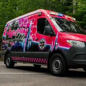A red and pink ambulance, converted into a wedding DJ service, parked in a parking lot.
