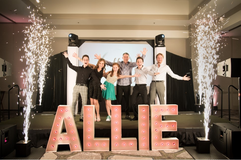 A group of people posing in front of a sign that says allie at a bar mitzvah.
