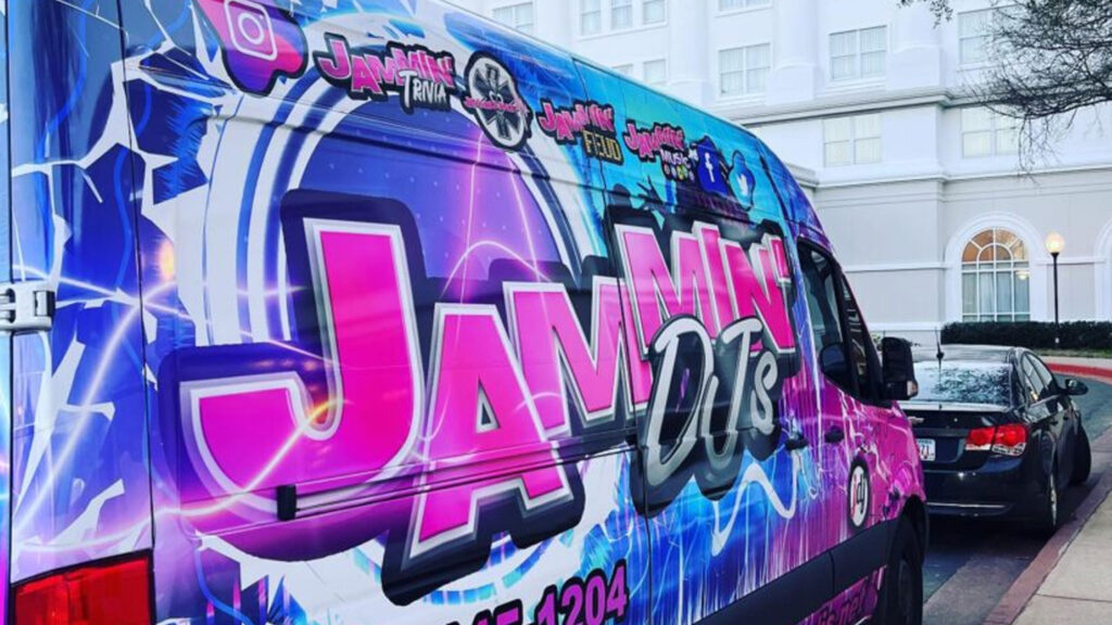 A van with a pink and purple design, featuring a Denver DJ logo, parked in front of a building.