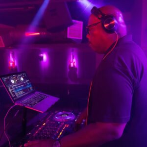A DJ with headphones in front of a laptop in a dark room, offering dj service for events.