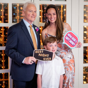 A man and woman posing for a photo in front of a wine cellar, at a bat mitzvah equipped with DJ service.