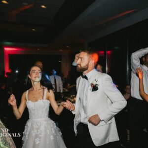 A bride and groom dance together at a wedding reception while guests sway in the background under colorful lights, creating a moving gallery of joyful moments.