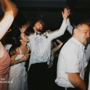 A group of people, dressed formally, dance with arms raised at a wedding celebration. The mood is jubilant with everyone appearing to enjoy themselves. A logo at the bottom left reads "Sound Originals.