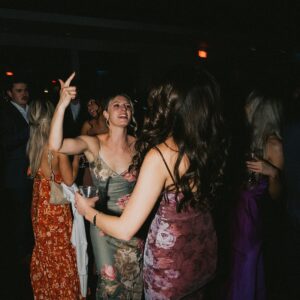 A group of people in formal attire dance and enjoy themselves at a wedding event under dim lighting. The atmosphere appears lively.