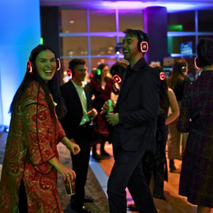 People wearing wireless headphones are dancing and socializing at a lively indoor silent disco event.