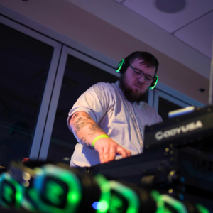 A DJ with neon headphones masterfully operates a DJ controller at the event, creating an electrifying vibe akin to a silent disco.