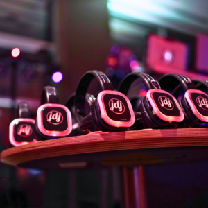 A row of black wireless headphones, glowing with red light, rests on a wooden table in a dimly lit room, ready for an unforgettable silent disco party.