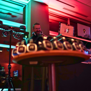A DJ spins tracks with equipment in the background while a table brims with small, round headphones for a silent disco. The room pulses with colorful lights, inviting you into the vibrant scene.