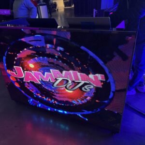 A DJ booth with a vibrant screen displaying the words "Jammin' DJs" and colorful graphics.