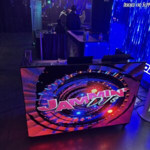 A vibrant digital display with "Jammin 107.5" illuminated in colorful graphics, set against a dark background with bright lights and people in the distance.