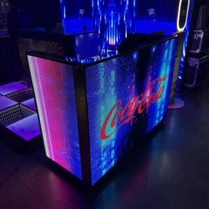 Coca-Cola branded kiosk with digital displays showing blue and red patterns, set up indoors with overhead lighting.