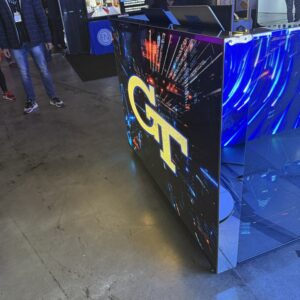 Display booth with "GT" logo on the screen, surrounded by people at an event.