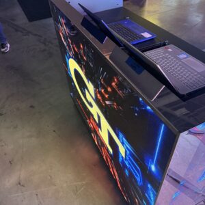 A high-tech booth with two laptops displayed on a reflective surface, surrounded by colorful digital graphics.