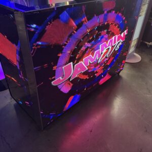 A colorful DJ booth with the text "Jammin DJ's" displayed on a screen, showing abstract red, blue, and purple patterns.