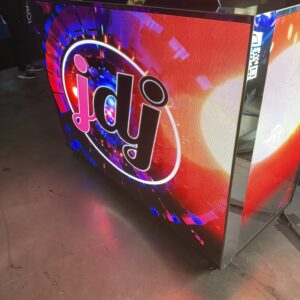 Illuminated DJ booth displaying a colorful digital logo with "jdj" in the center, set against an energetic, abstract background.