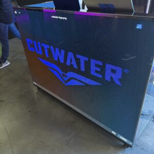 Large screen displaying the Cutwater logo in purple, positioned on a stand in an exhibition space.