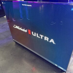Display screen showing the Michelob Ultra logo with reflections visible on the floor and nearby items.