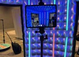 A tablet on a stand captures the image of an illuminated room with blue and multicolored LED light panels on the walls, perfectly showcasing a vibrant atmosphere ideal for a Denver Wedding and Events DJ Service.